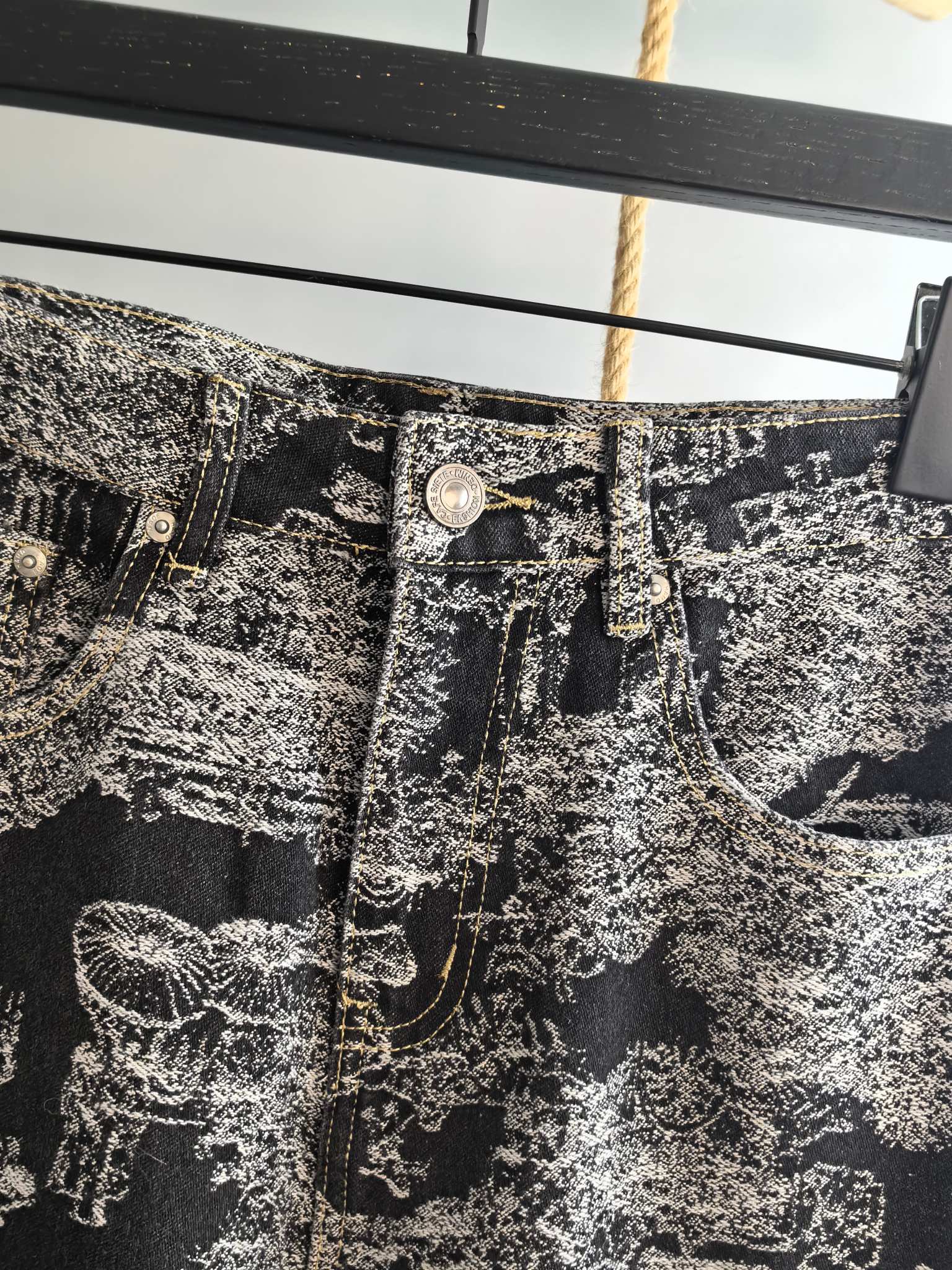 Close-up of black-and-white abstract printed pants waistband with metal button details