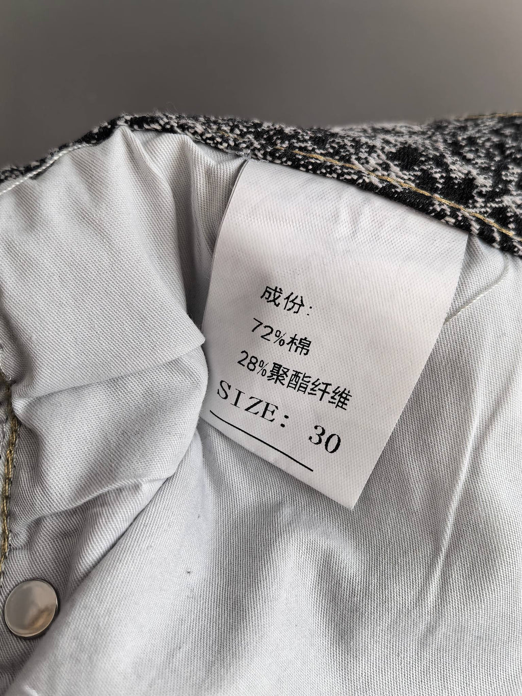 Fabric care label inside black-and-white printed pants, with size and composition text