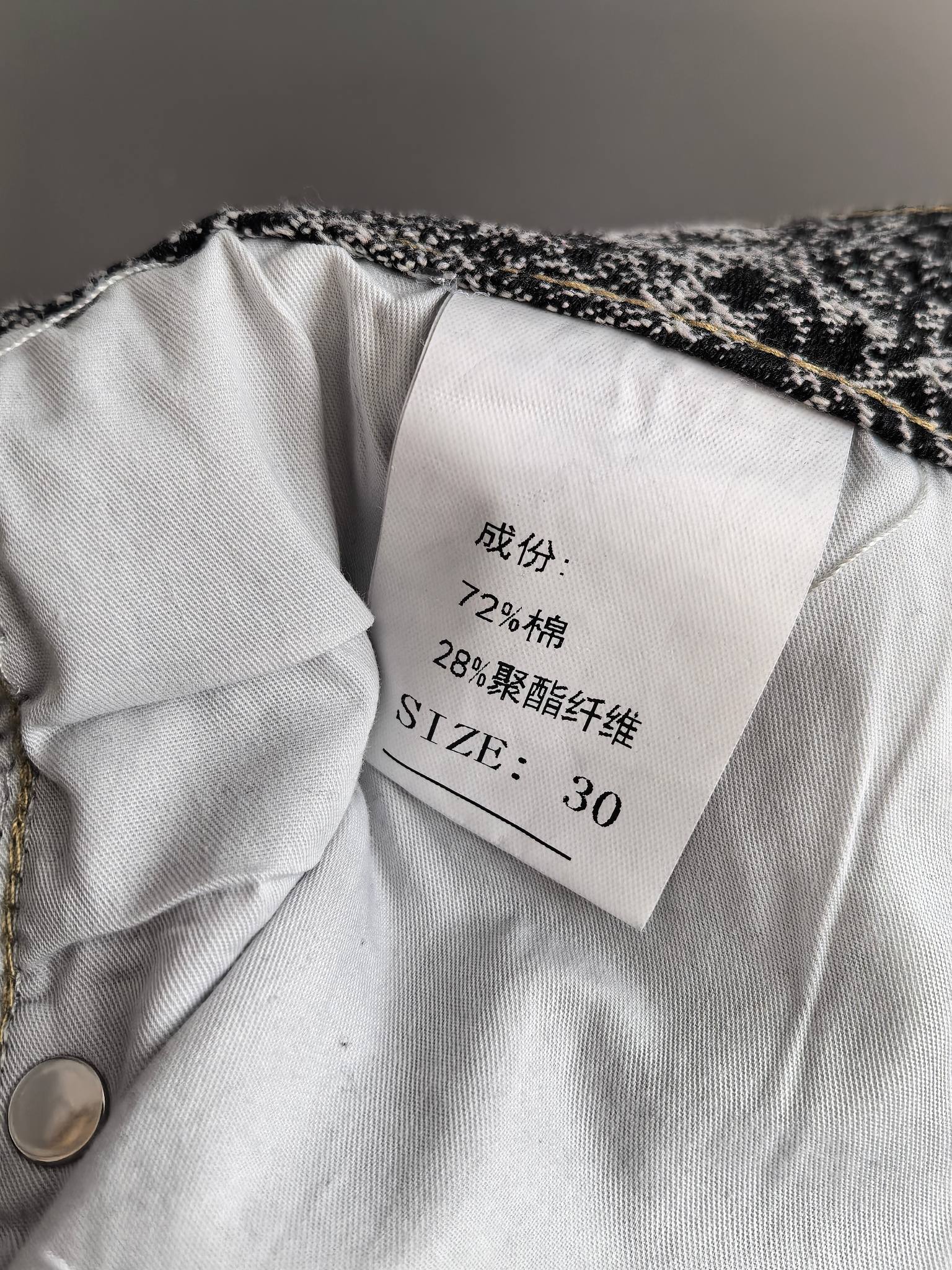 Fabric care label inside black-and-white printed pants, with size and composition text