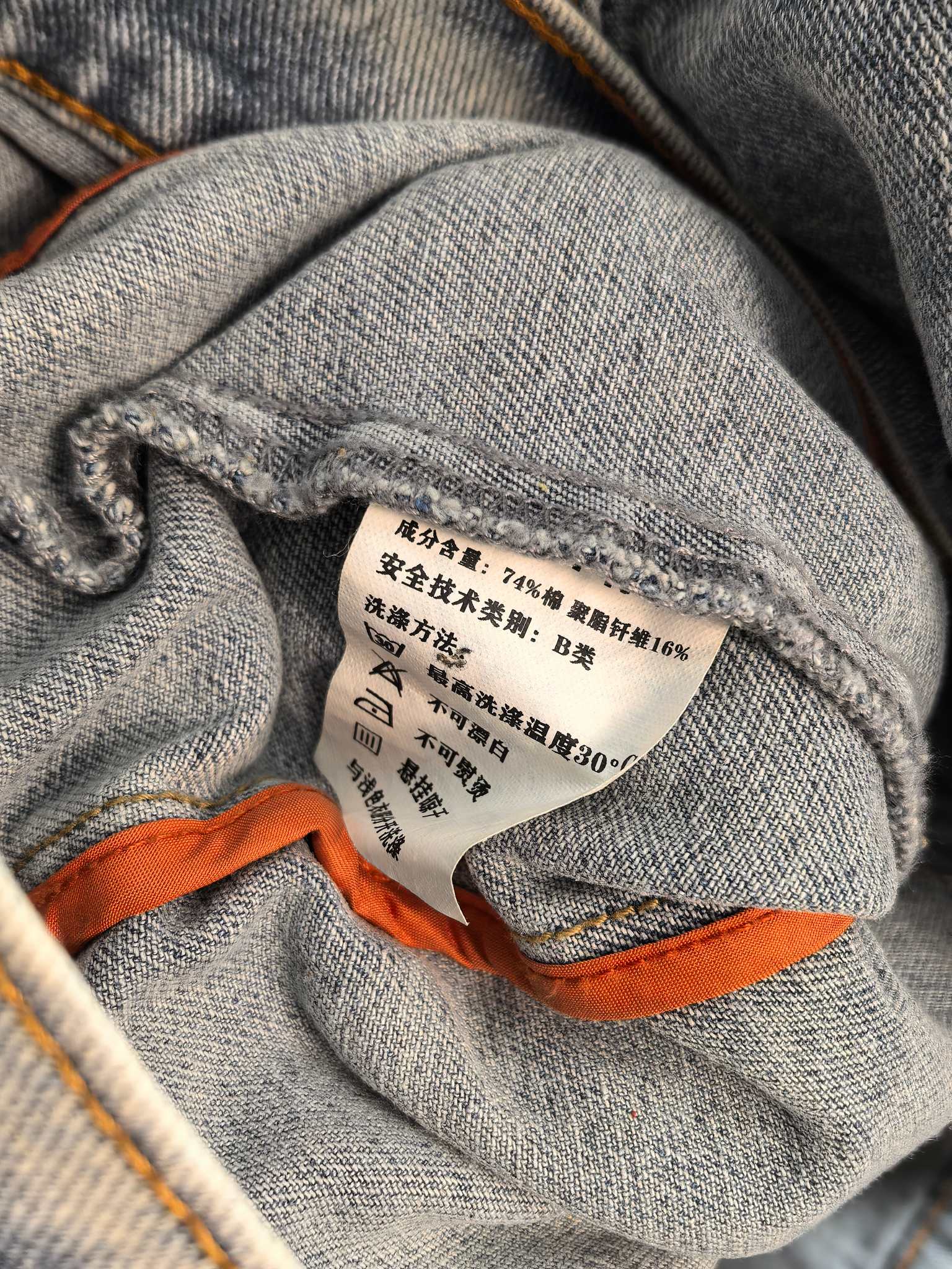 Denim jacket interior fabric label inside seam with orange trim