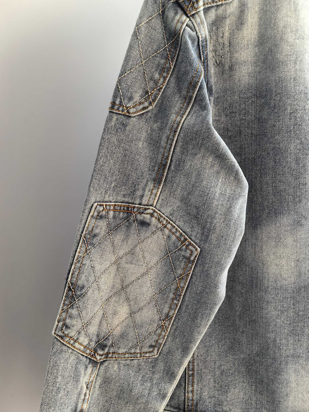 Denim jacket side with quilted patch pocket and stitched seam, light blue wash