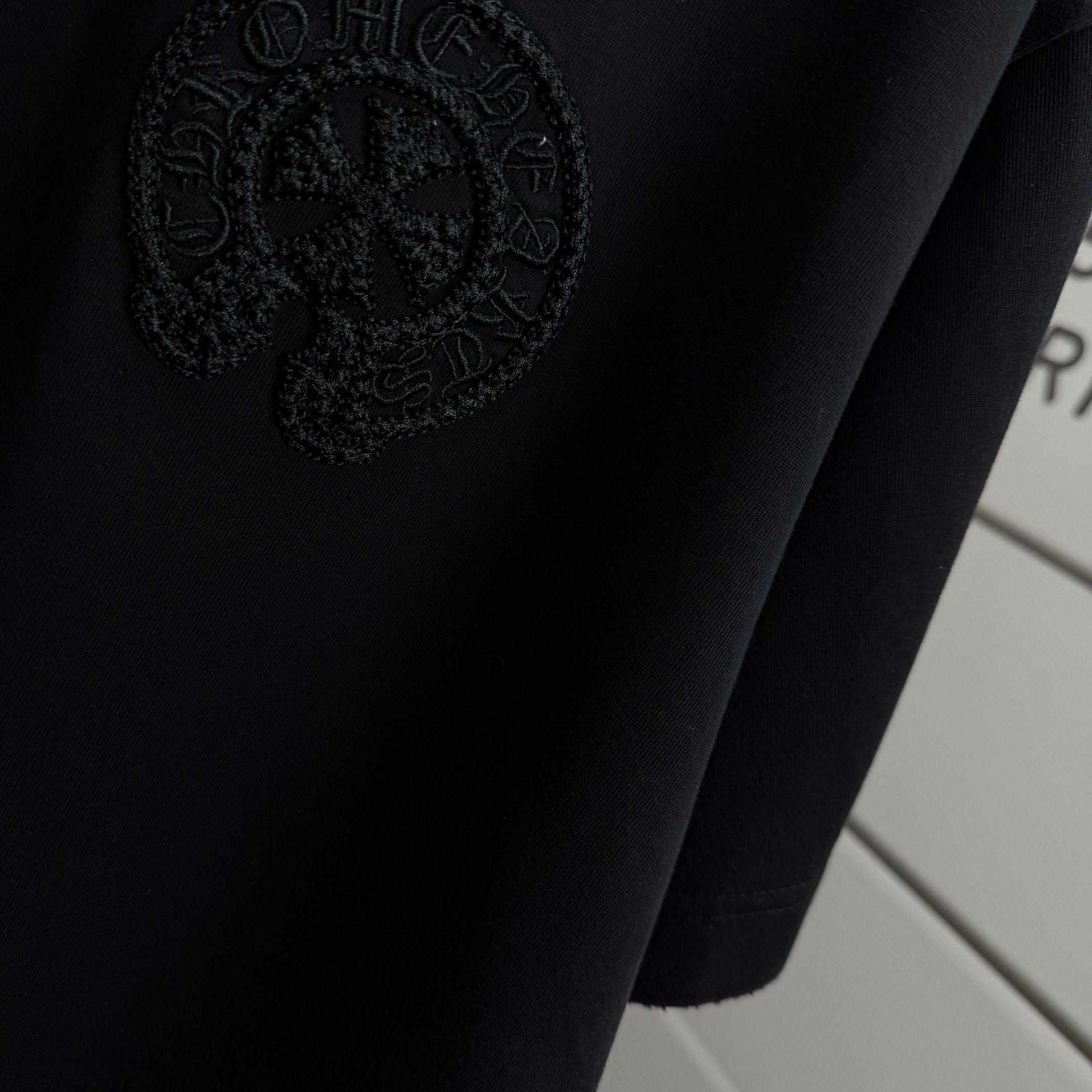 Black short-sleeve T-shirt with embossed circular logo detail near hem