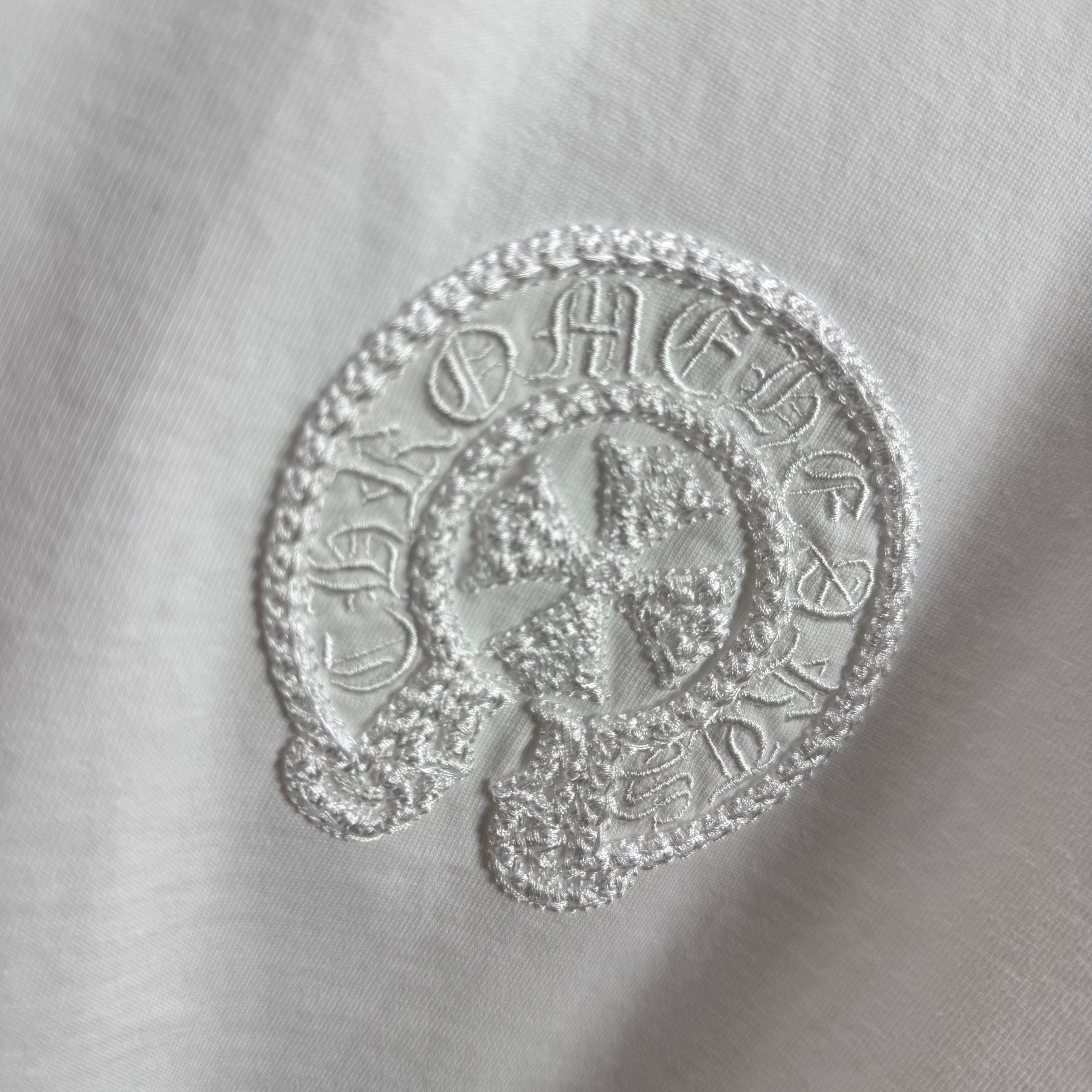 Light T-shirt with textured circular embroidered logo detail.