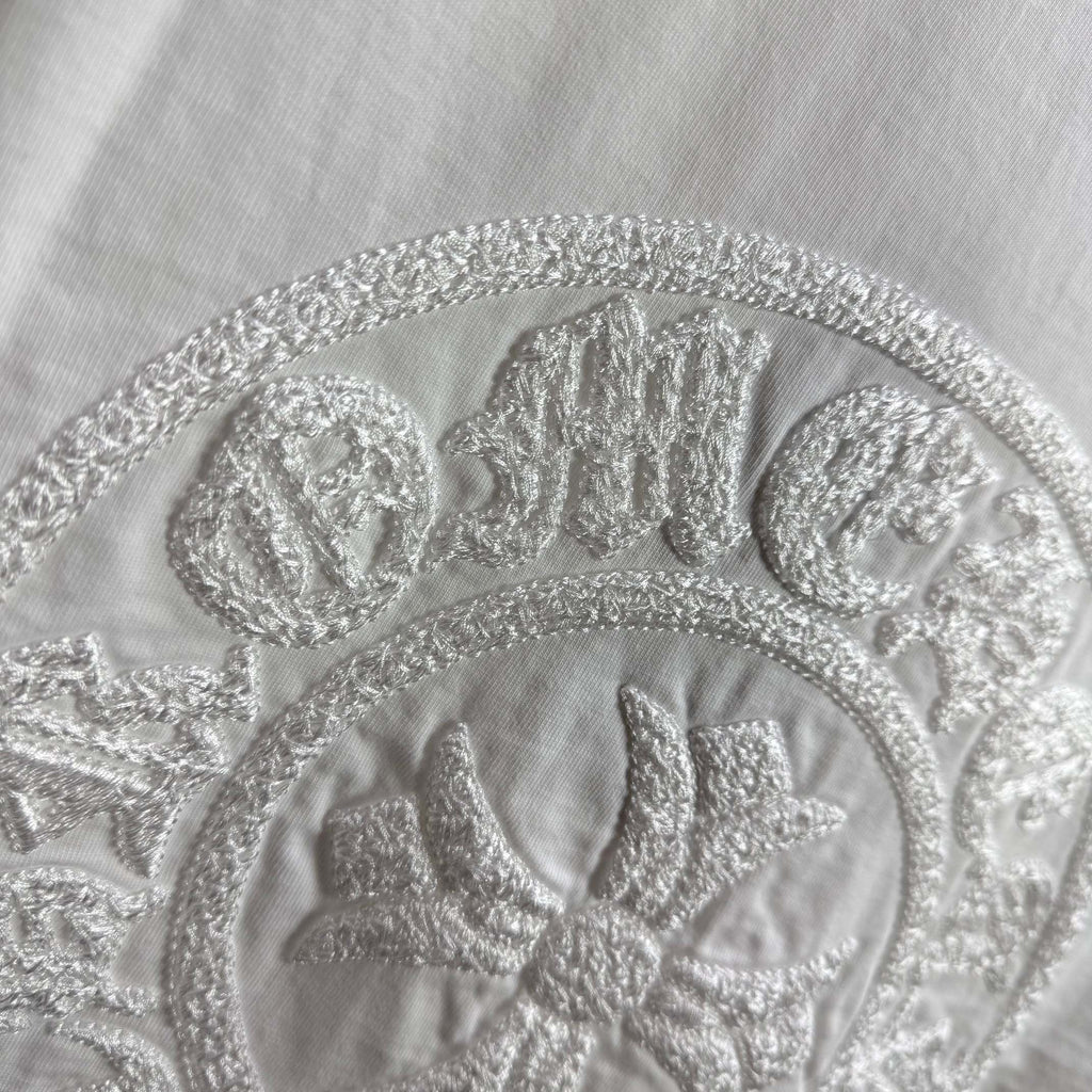 Light T-shirt close-up of circular embroidered crest logo and detailing.