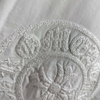 Light T-shirt close-up of circular embroidered crest logo and detailing.