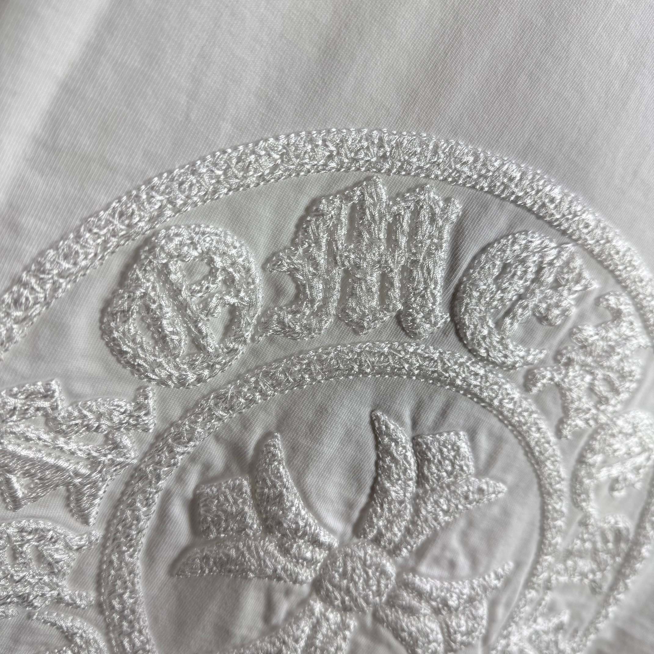 Light T-shirt close-up of circular embroidered crest logo and detailing.
