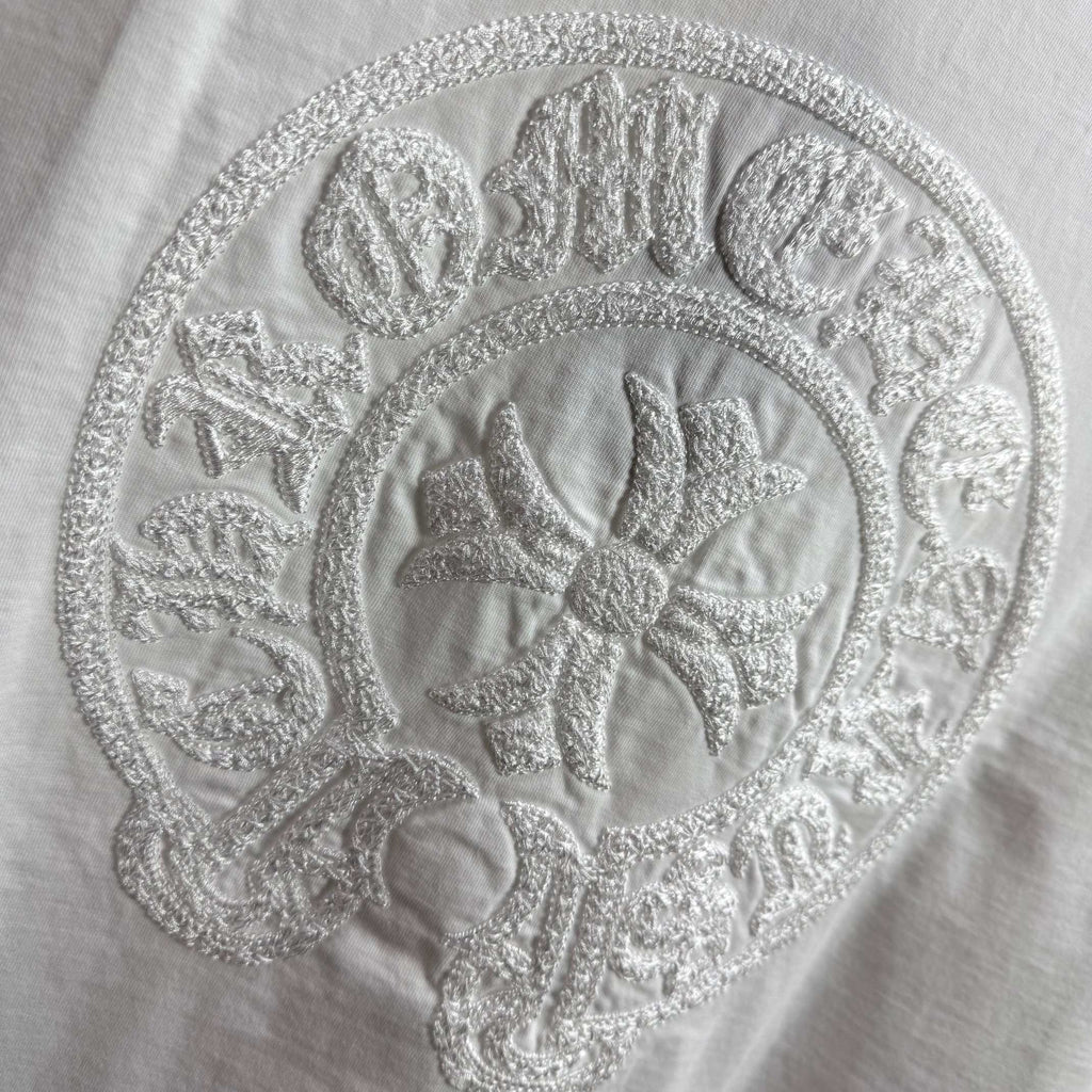 Light T-shirt with close-up circular embroidered crest logo.