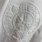 Light T-shirt with close-up circular embroidered crest logo.