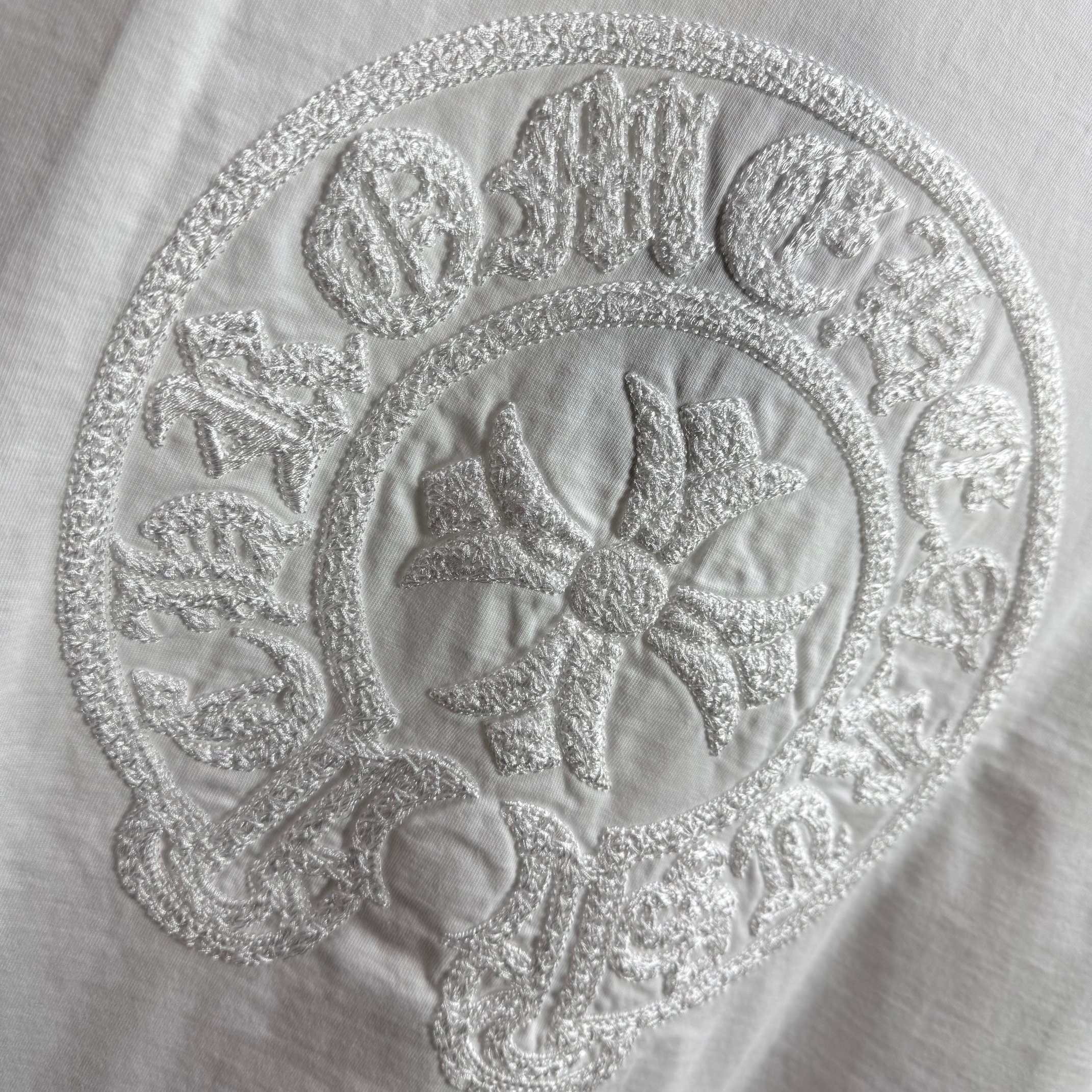 Light T-shirt with close-up circular embroidered crest logo.
