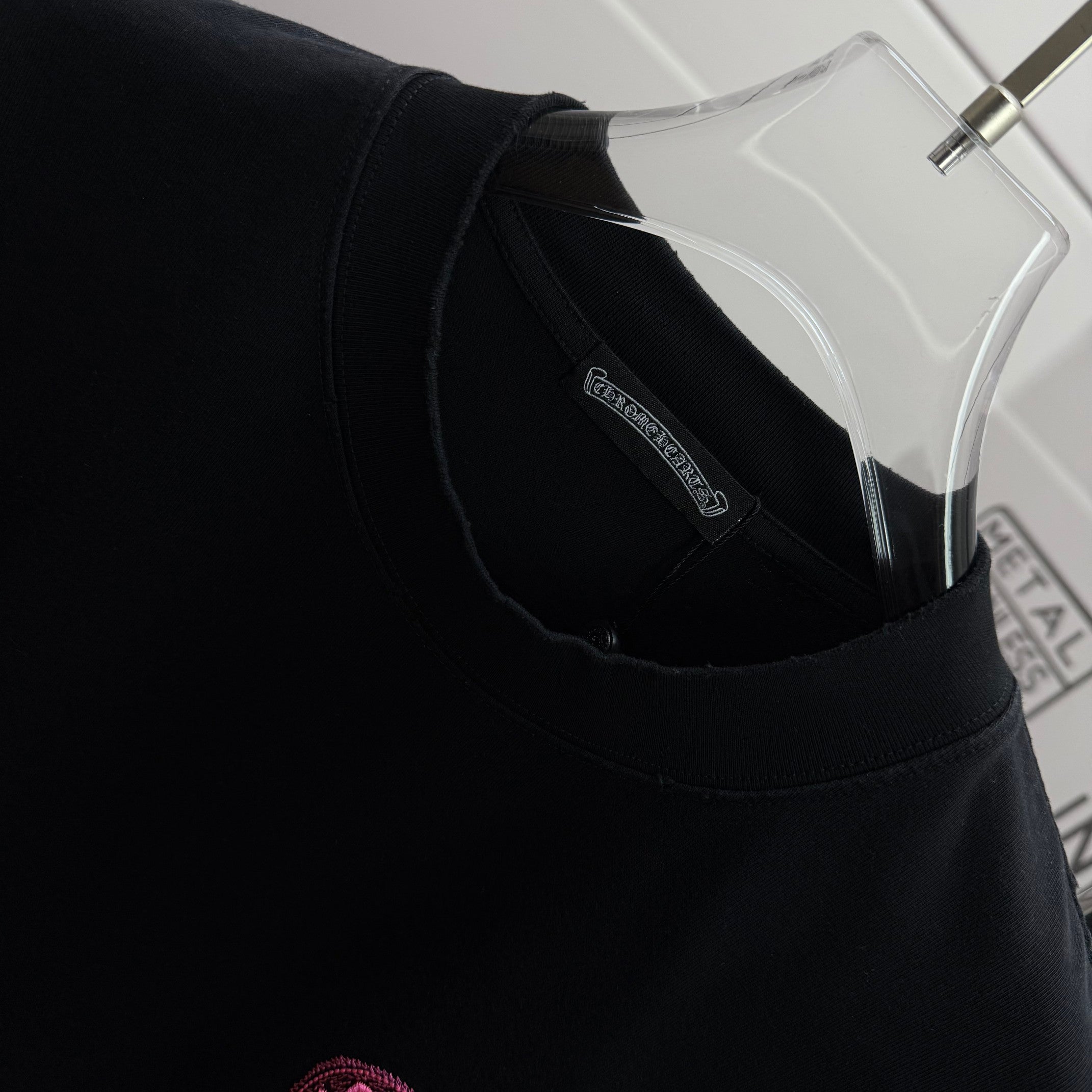 Black T-shirt neckline with inner collar label and pink embroidered chest icon