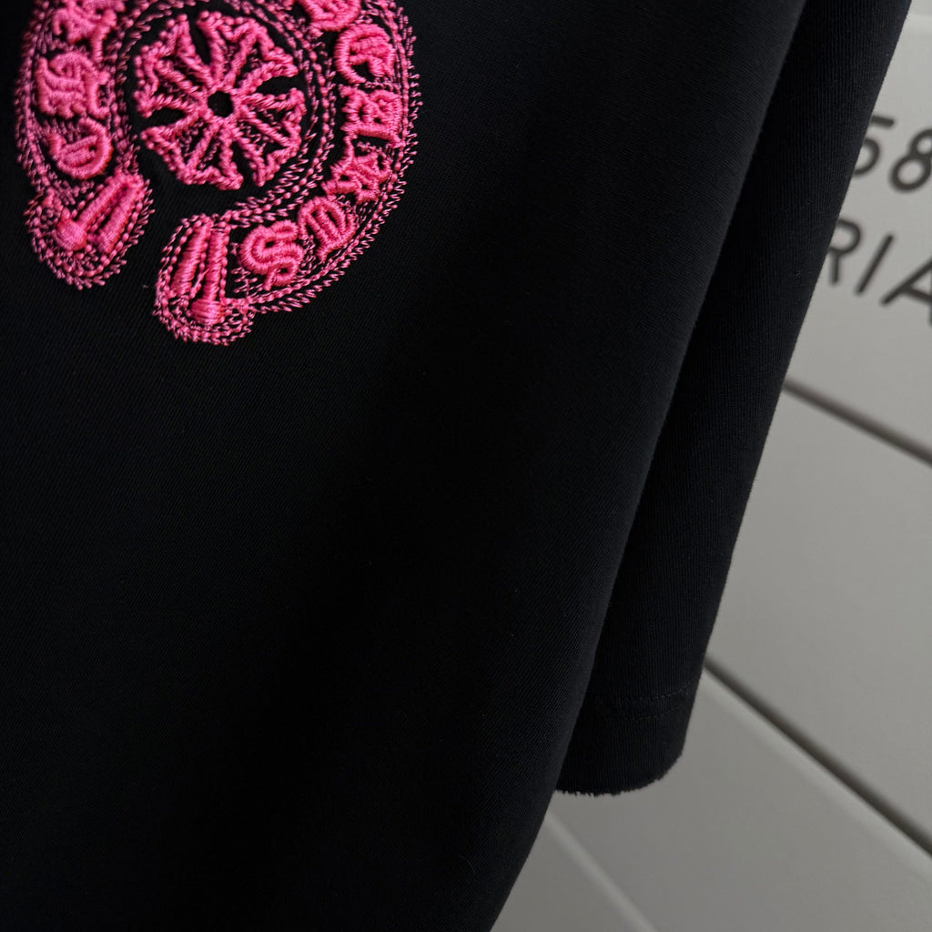 Black T-shirt with pink embroidered logo patch on upper chest