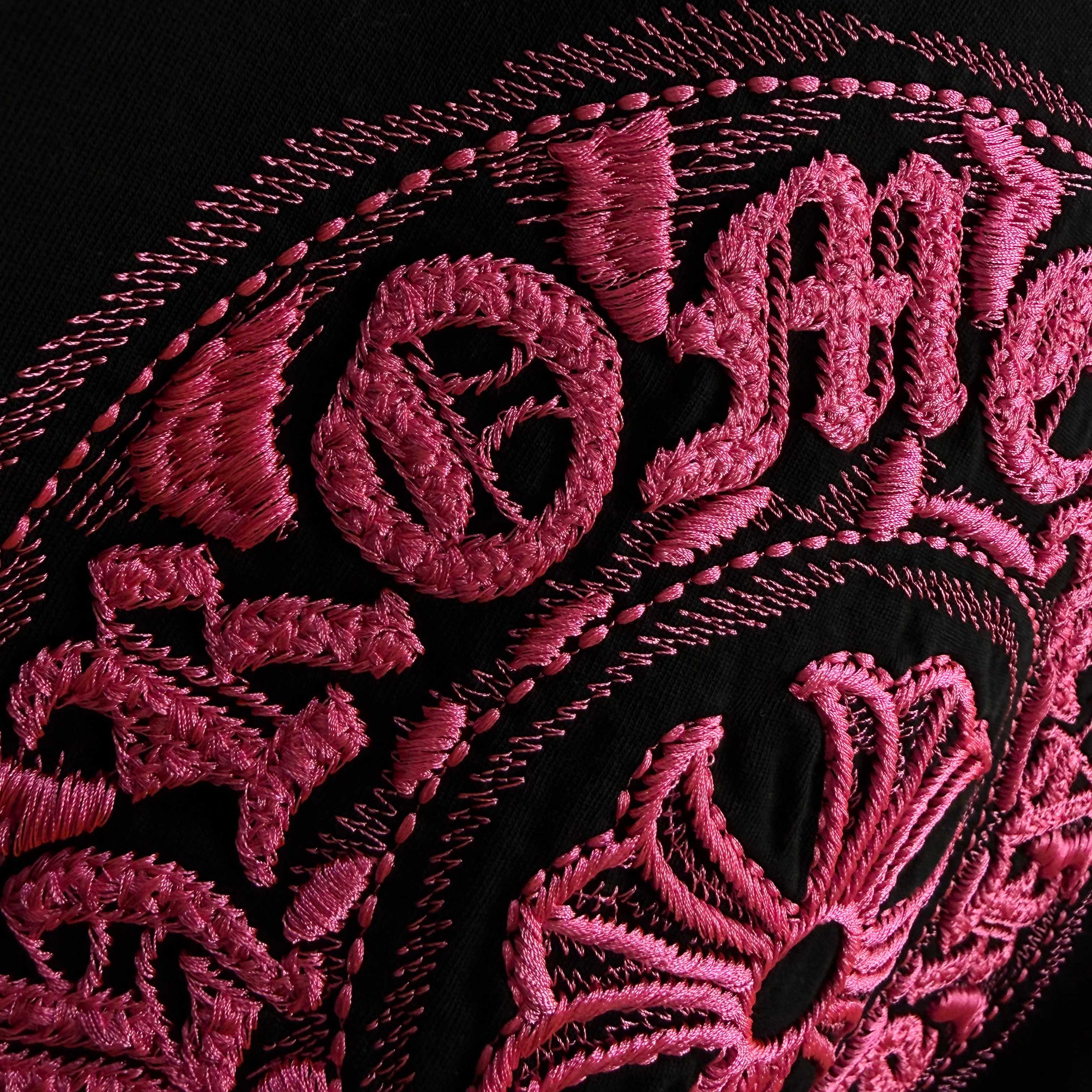 Black T-shirt close-up with pink embroidered lettering and circular emblem