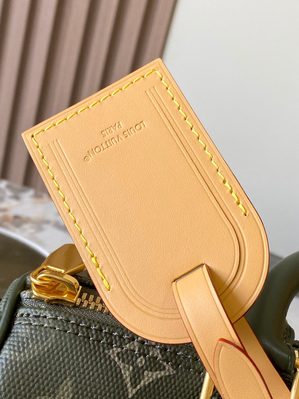 Close-up of tan leather strap tag attached to green monogram handbag hardware.
