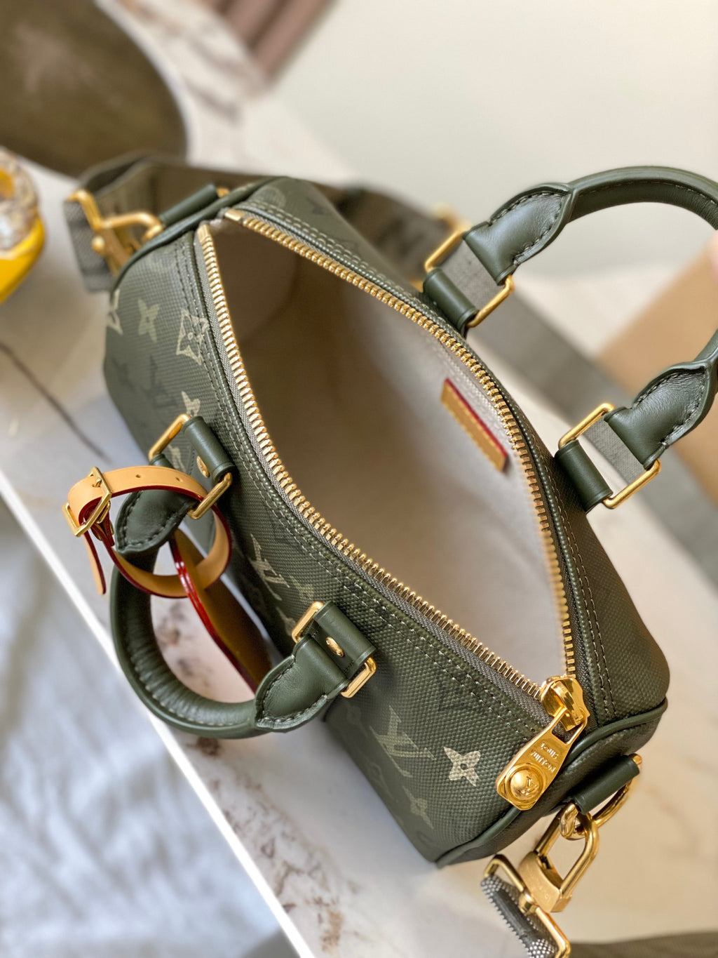 Green monogram handbag open top with interior lining and gold zipper hardware.