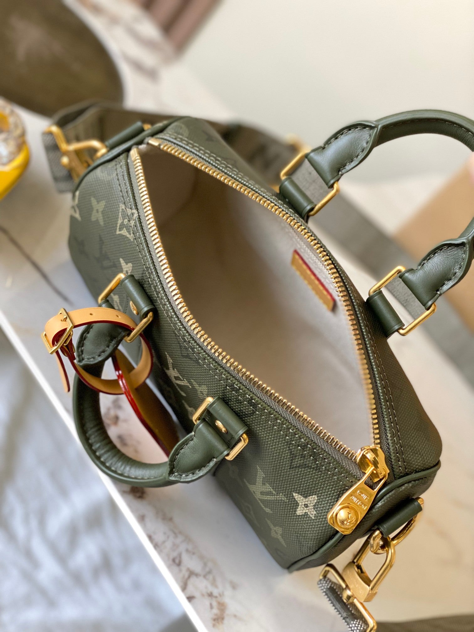 Green monogram handbag open top with interior lining and gold zipper hardware.