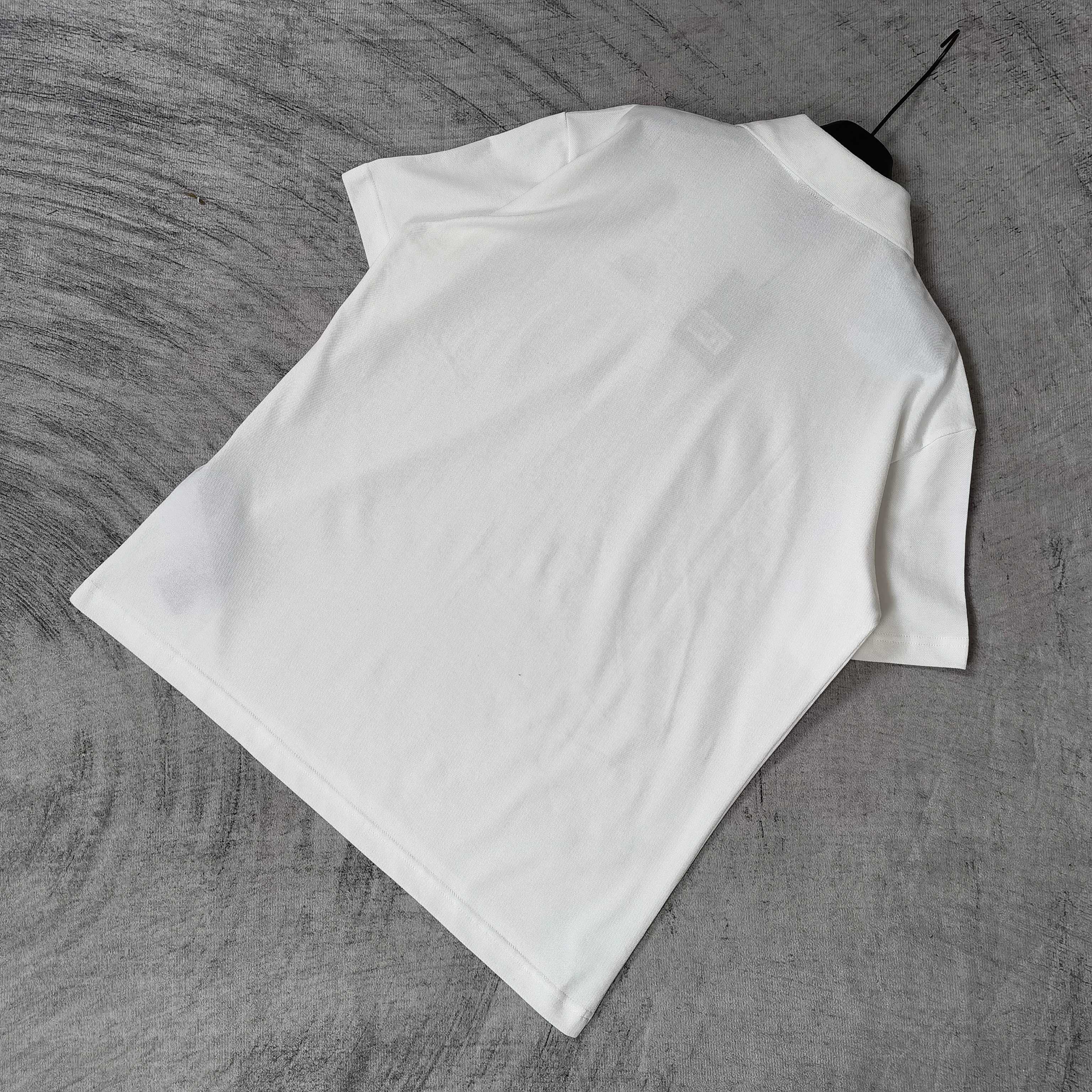 Balenciaga white polo shirt laid flat, short sleeves, collar and button edge visible