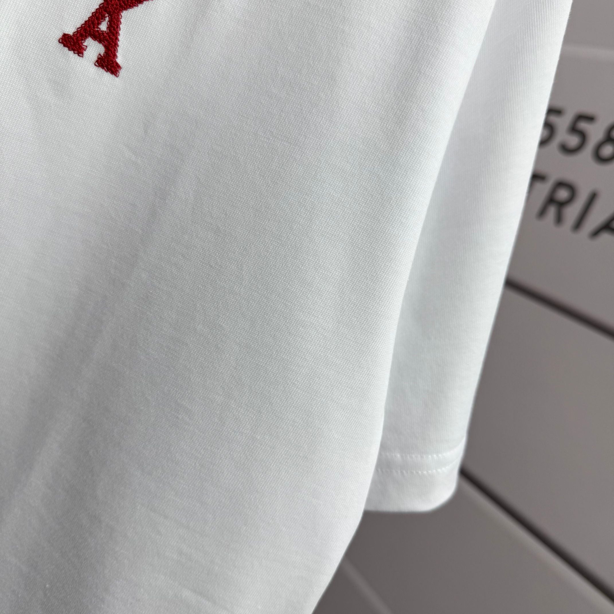Amiri white T-shirt fabric close-up with partial red heart-and-A logo near shoulder