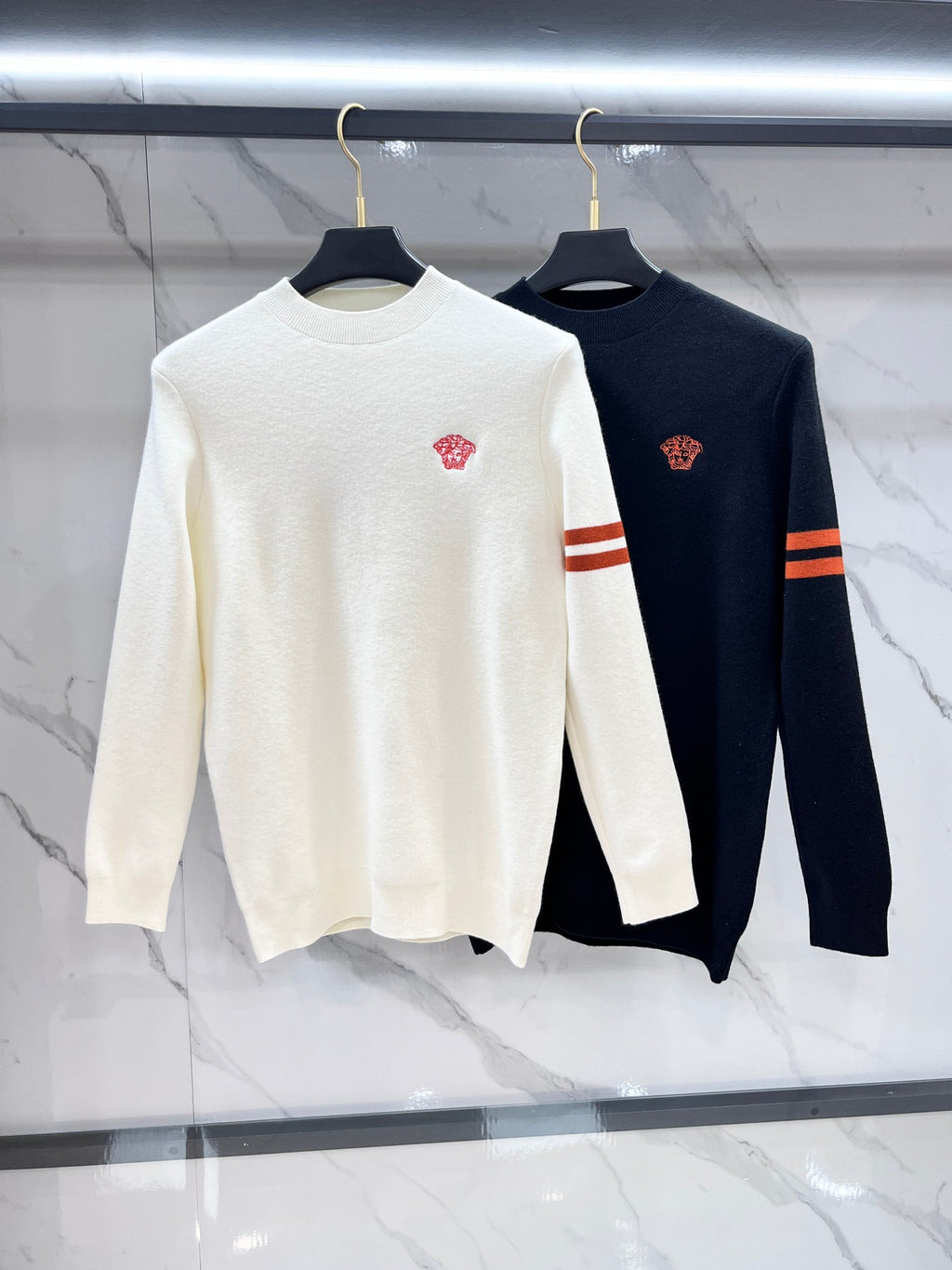 Pair of knit sweaters on hangers: white and dark navy, crewneck with red chest crest