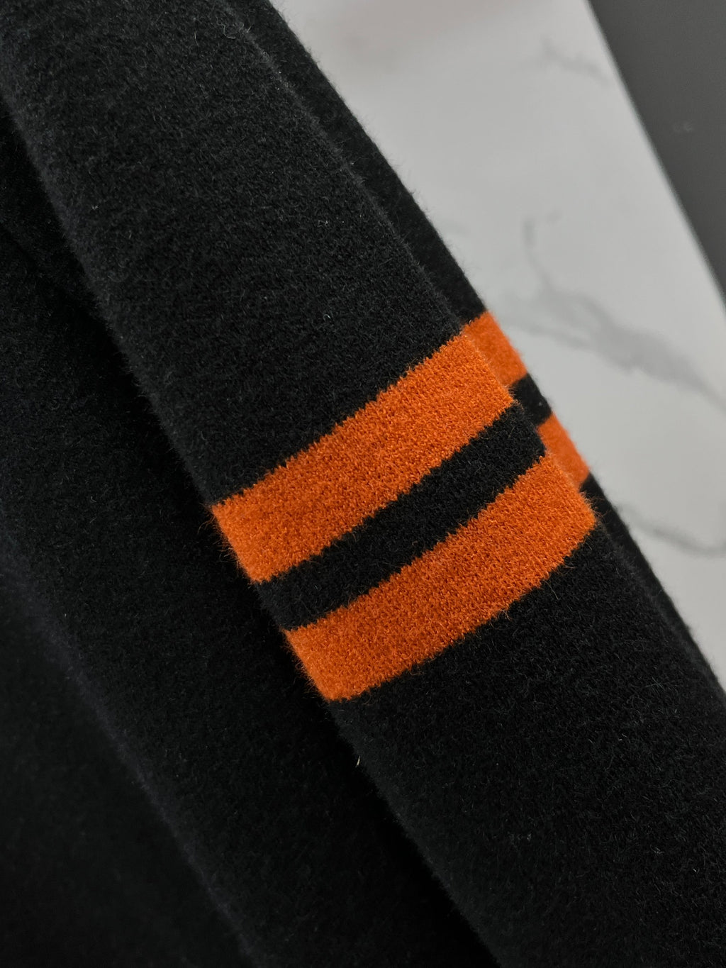 Black knit sweater sleeve with orange and black striped cuff detail