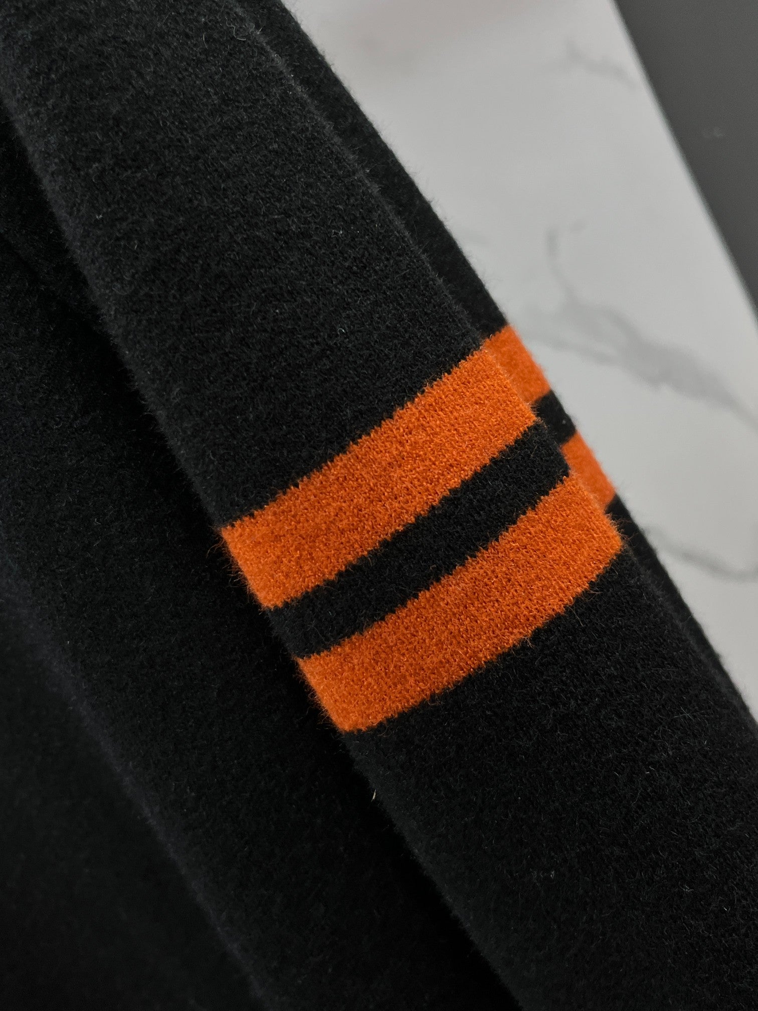 Black knit sweater sleeve with orange and black striped cuff detail