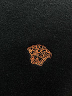 Black knit sweater with small orange embroidered crest emblem on fabric