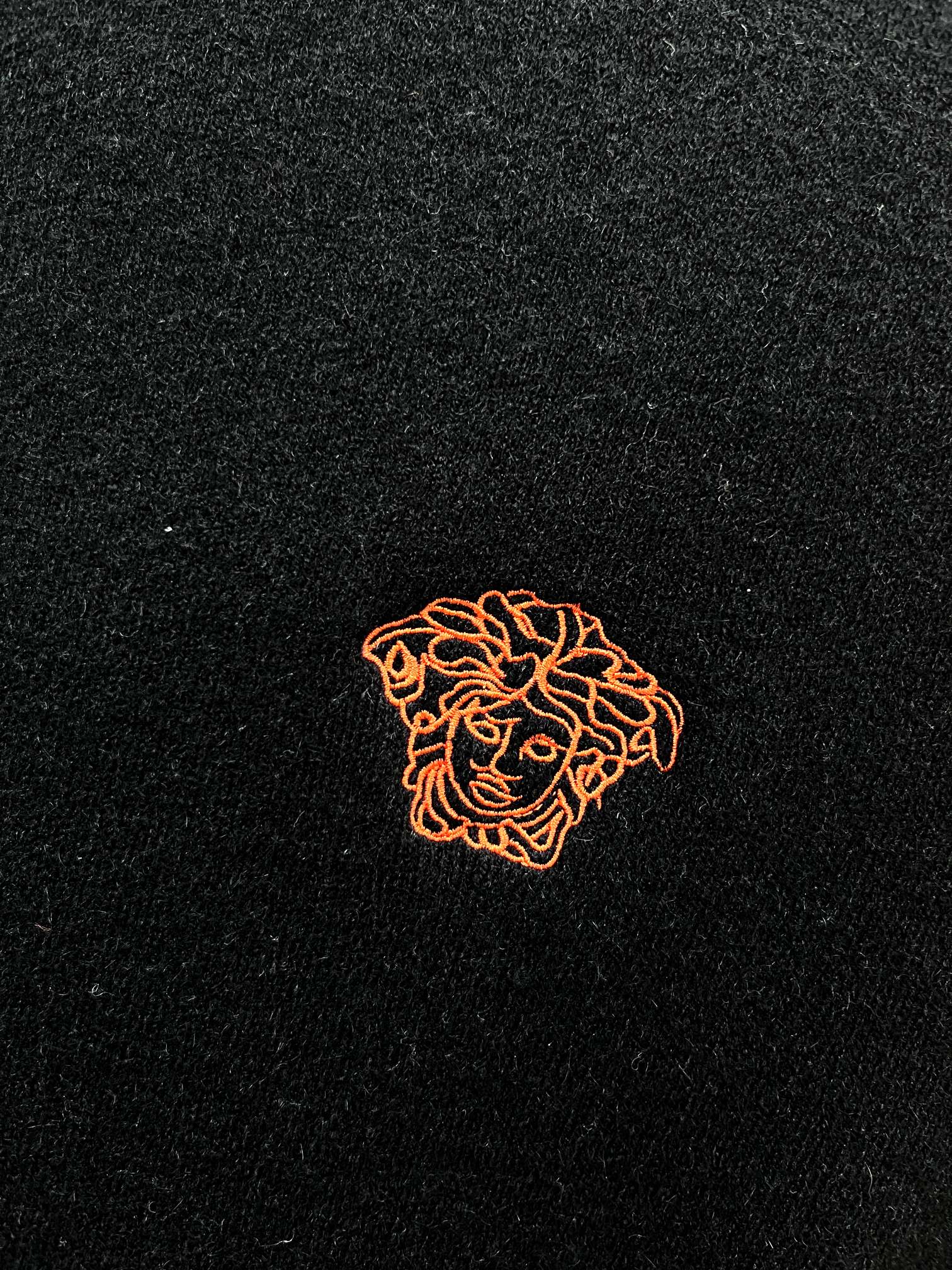 Black knit sweater with small orange embroidered crest emblem on fabric