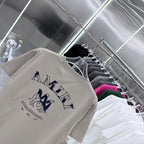 Light gray crewneck T-shirt with navy AMIRI letters and logo graphic on front