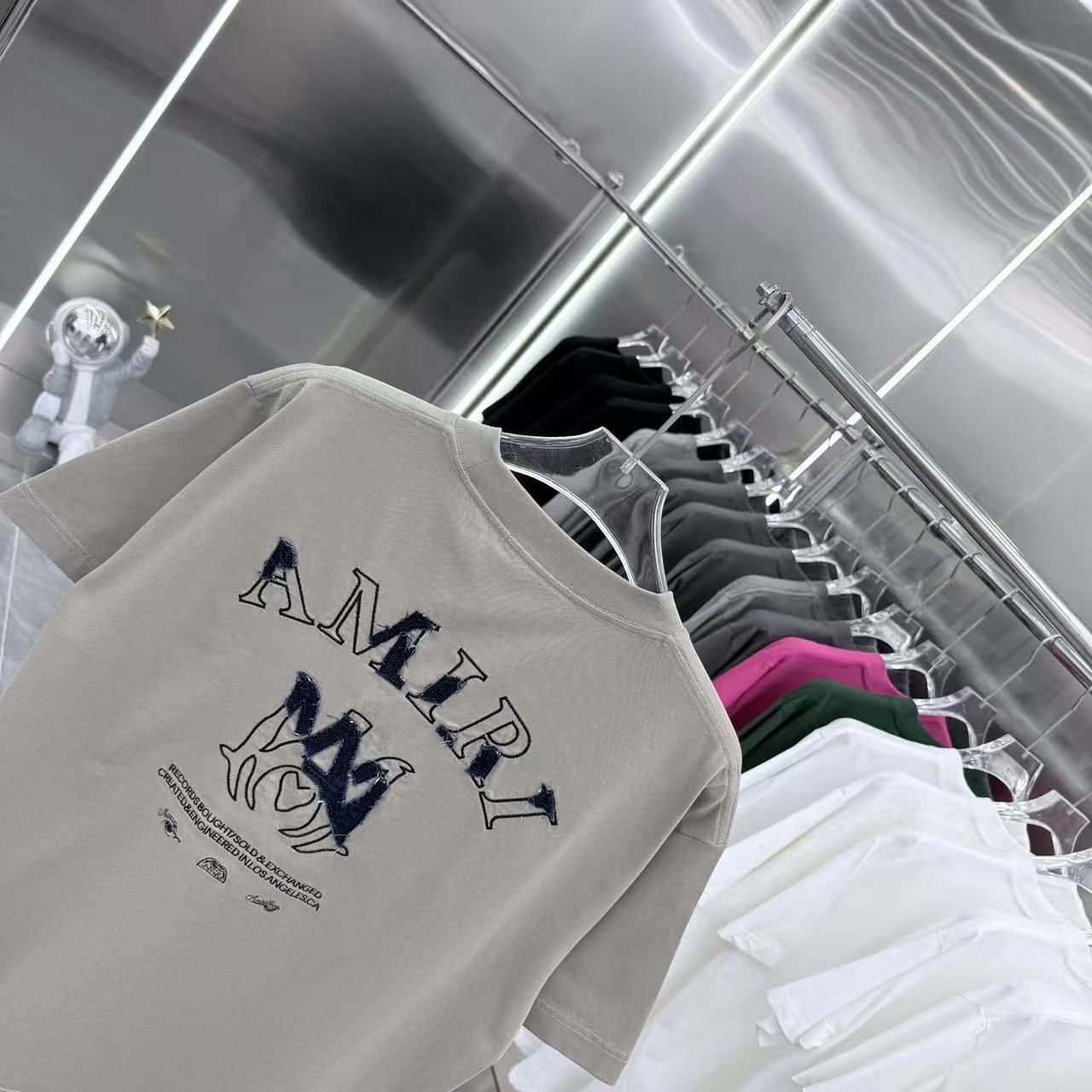 Light gray crewneck T-shirt with navy AMIRI letters and logo graphic on front