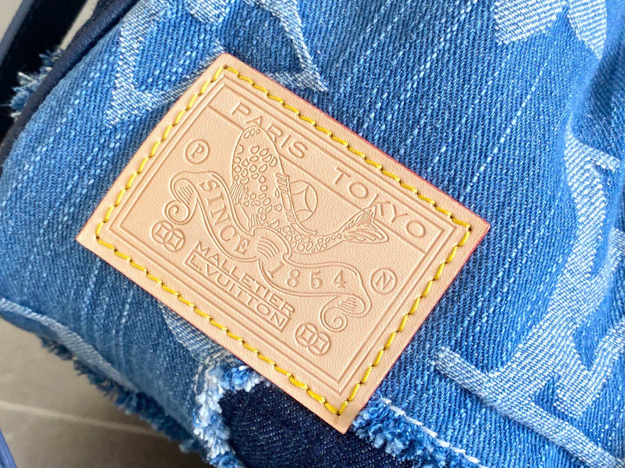 Blue patchwork denim bag with tan leather logo label on a fabric patch
