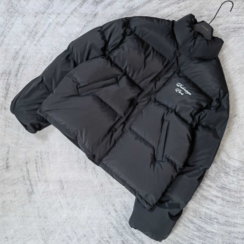 Long puffer jacket in dark gray, laid flat, with visible hood and logo patch