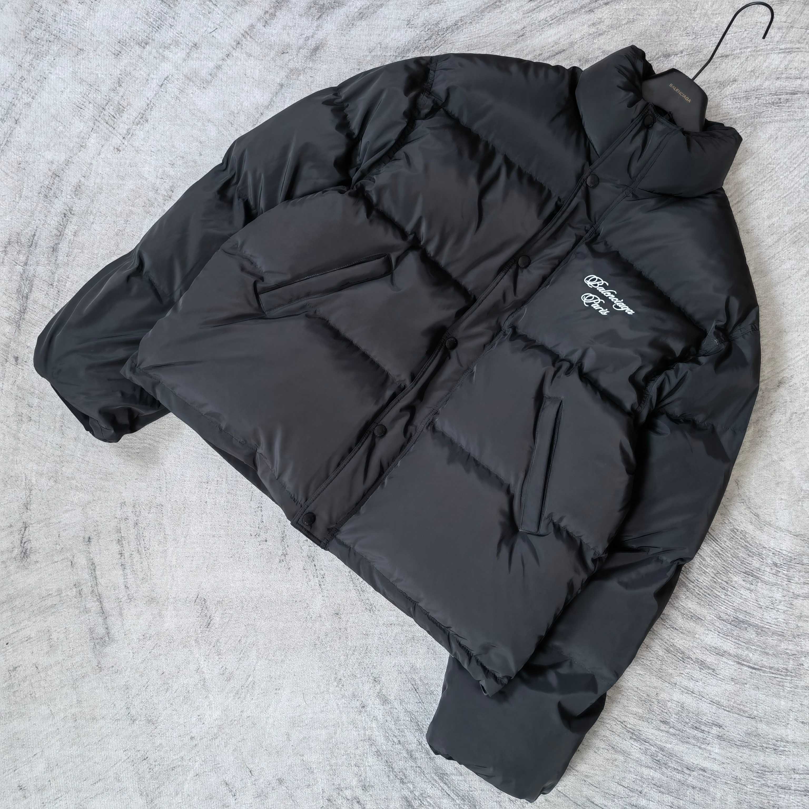 Long puffer jacket in dark gray, laid flat, with visible hood and logo patch