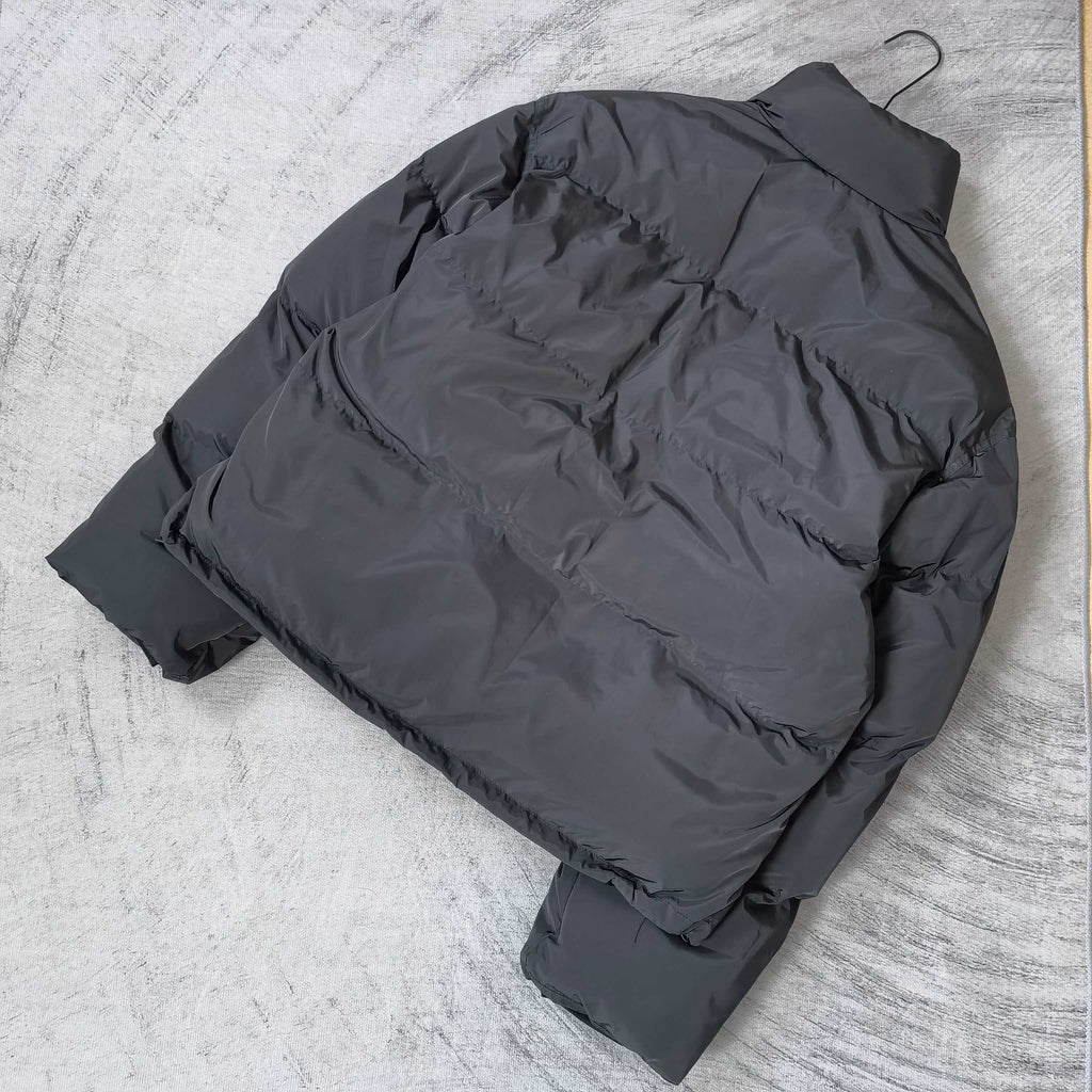 Long puffer jacket in dark gray, laid flat, showing quilted panels and hood