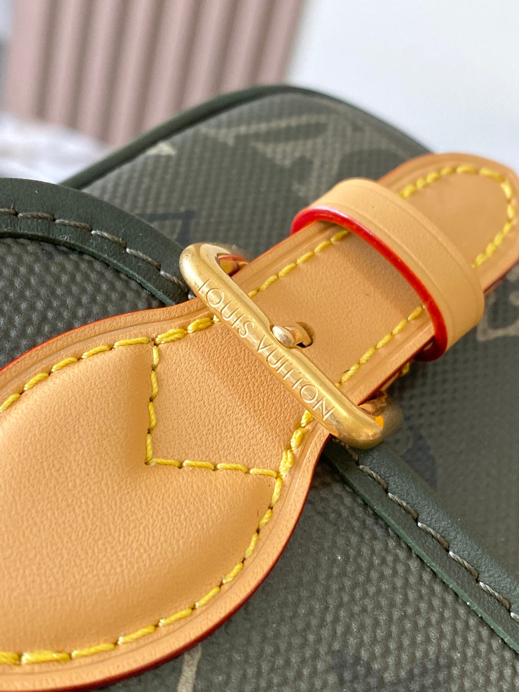 Louis Vuitton crossbody strap detail with tan leather trim and gold buckle on dark green canvas