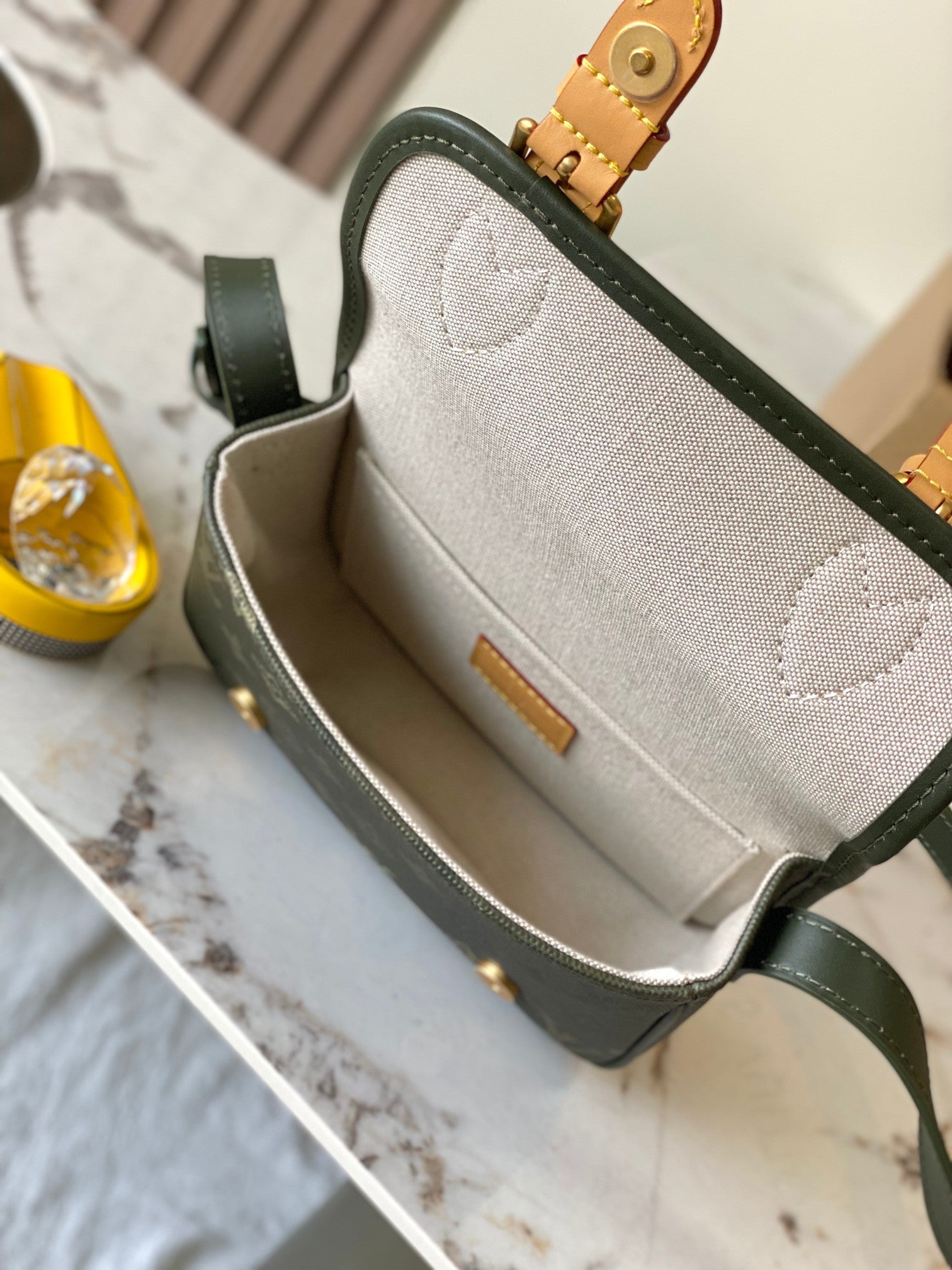 Open dark green Louis Vuitton crossbody showing beige interior lining and inner pocket.