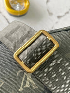 Louis Vuitton strap attachment close-up with gold buckle on dark green monogram canvas
