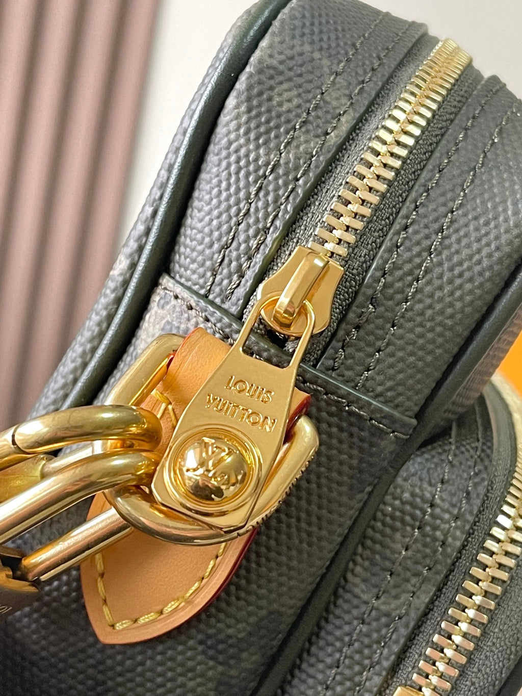 Louis Vuitton zipper pull and ring close-up with gold tag on dark green canvas