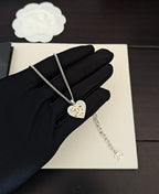 Silver-tone chain necklace with heart pendant on black gloves