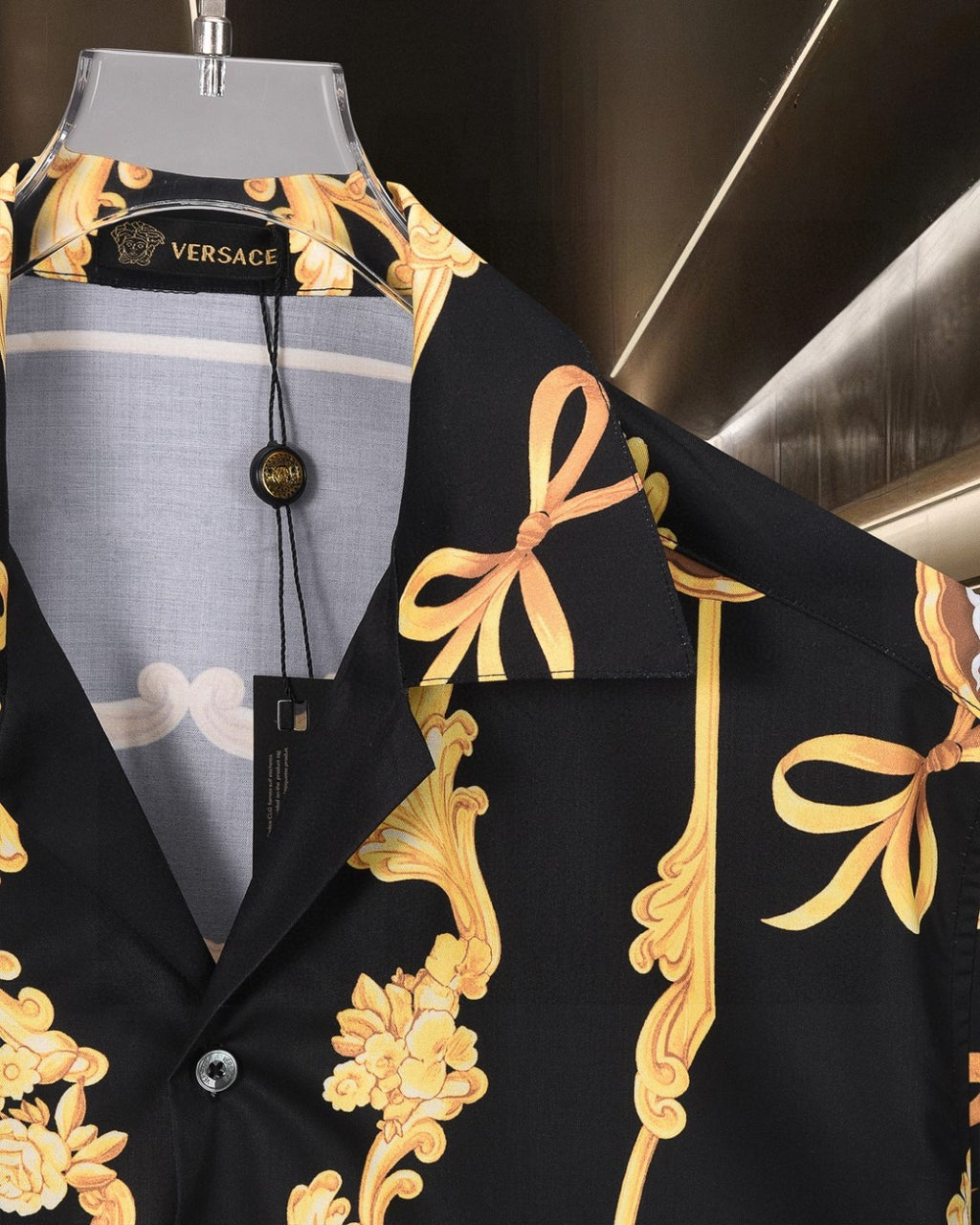 Black shirt detail at chest with gold floral scroll design and draped bow motif
