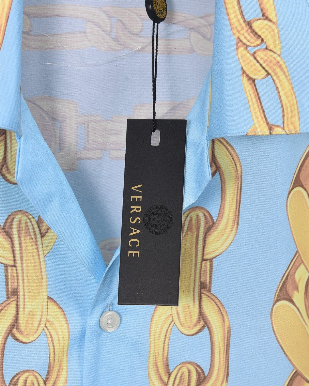 Versace clothing label on light blue shirt with gold chain print, black hanging tag