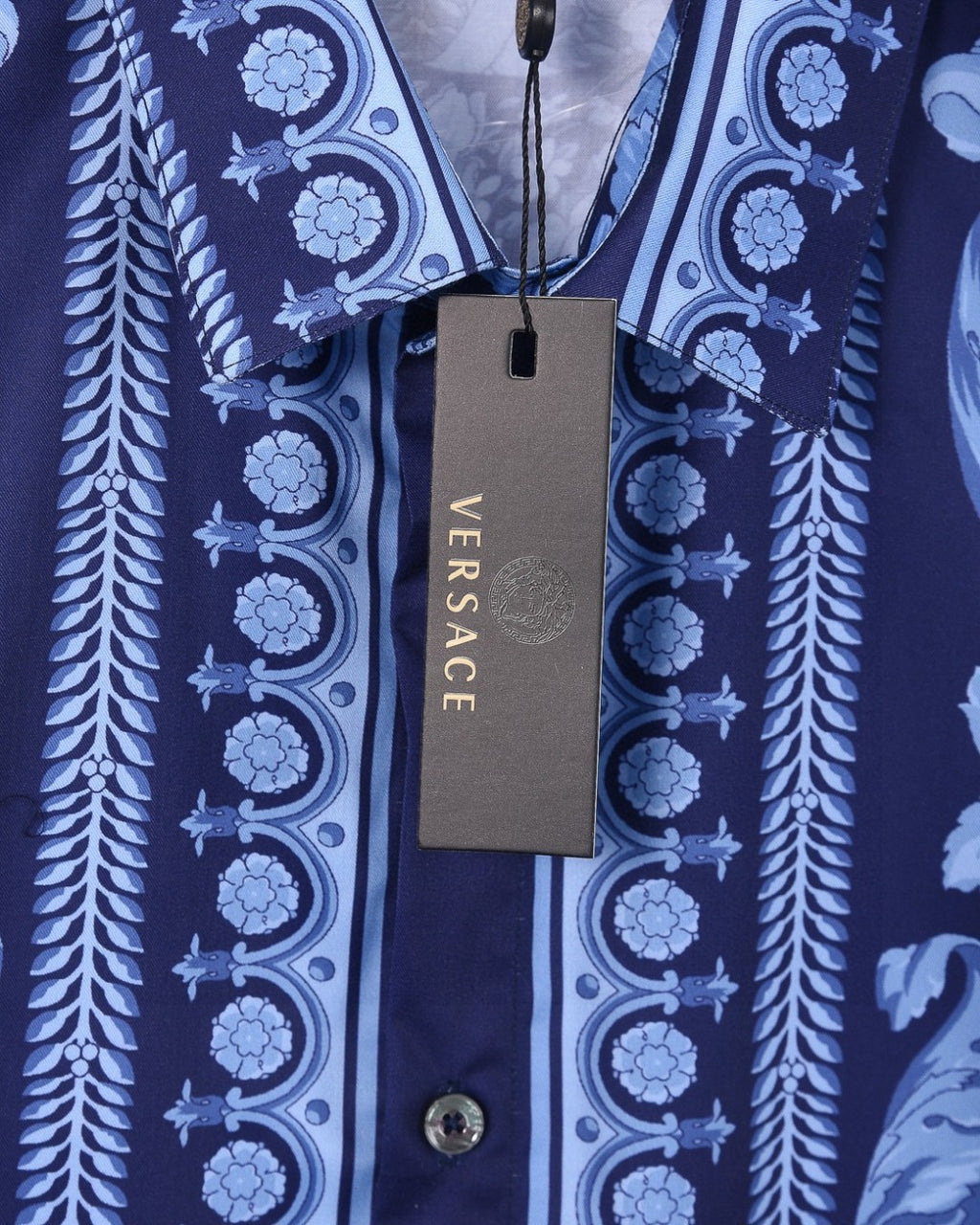Versace blue shirt hanging tag over patterned fabric and buttoned center placket