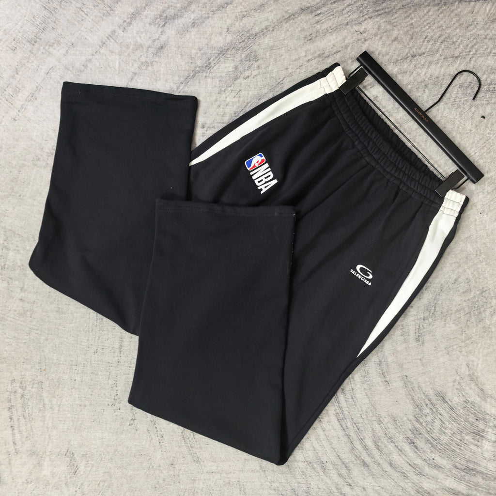 Black track pants laid flat, elastic waistband and white side stripe trim
