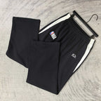 Black track pants laid flat, elastic waistband and white side stripe trim