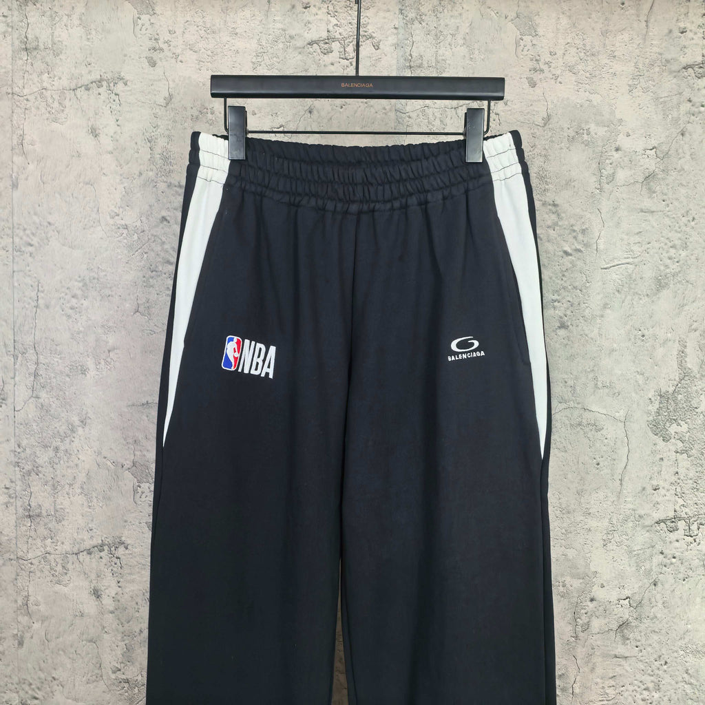 Black track pants with white side stripes, elastic waistband, NBA and Balenciaga logos
