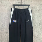 Black track pants with white side stripes, elastic waistband, NBA and Balenciaga logos