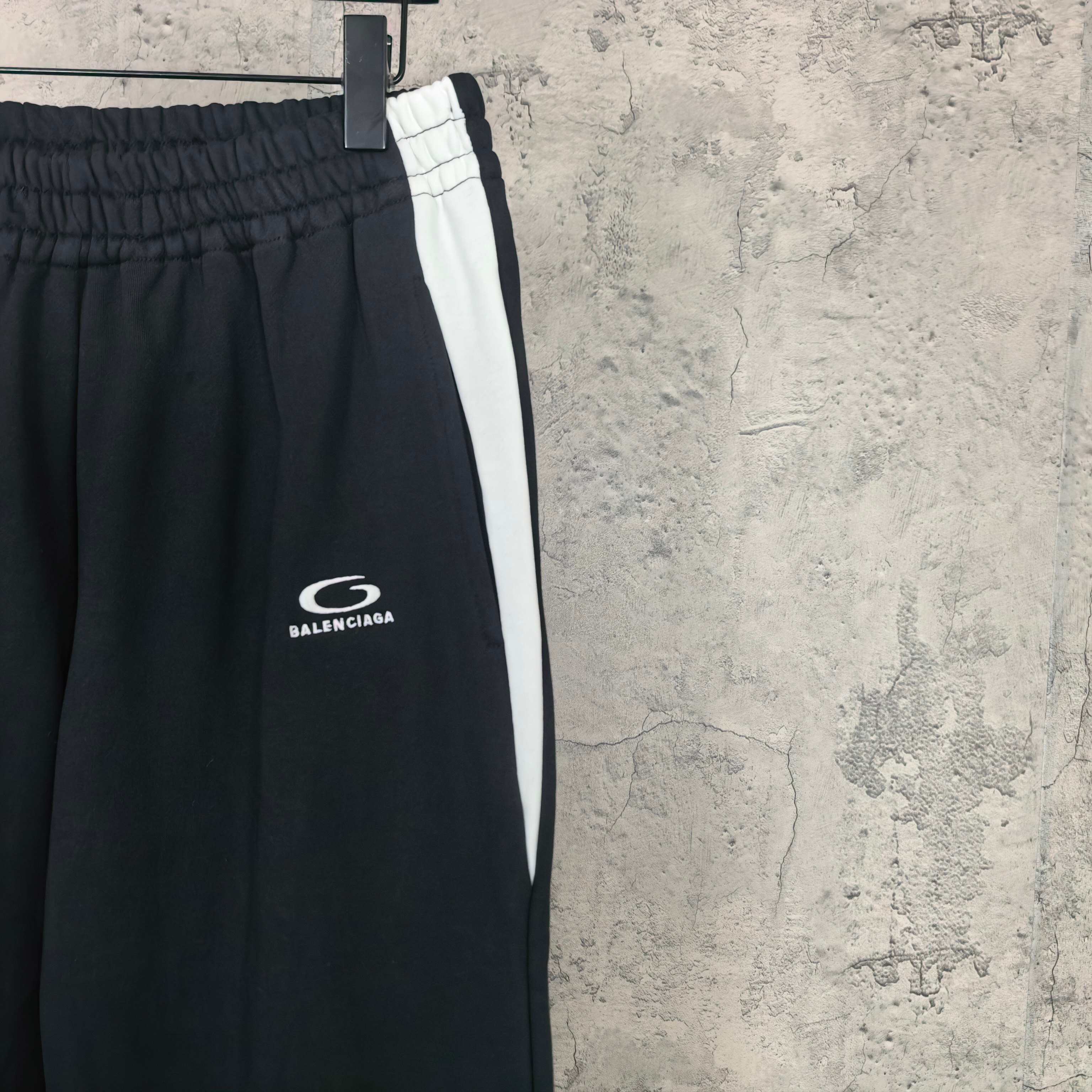 Black track pants with white side stripe and Balenciaga logo near thigh