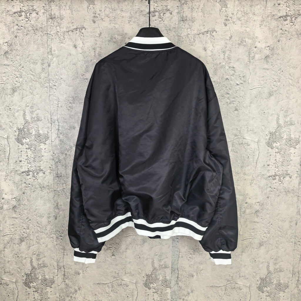 Black varsity bomber jacket, back view, with white striped ribbed hem