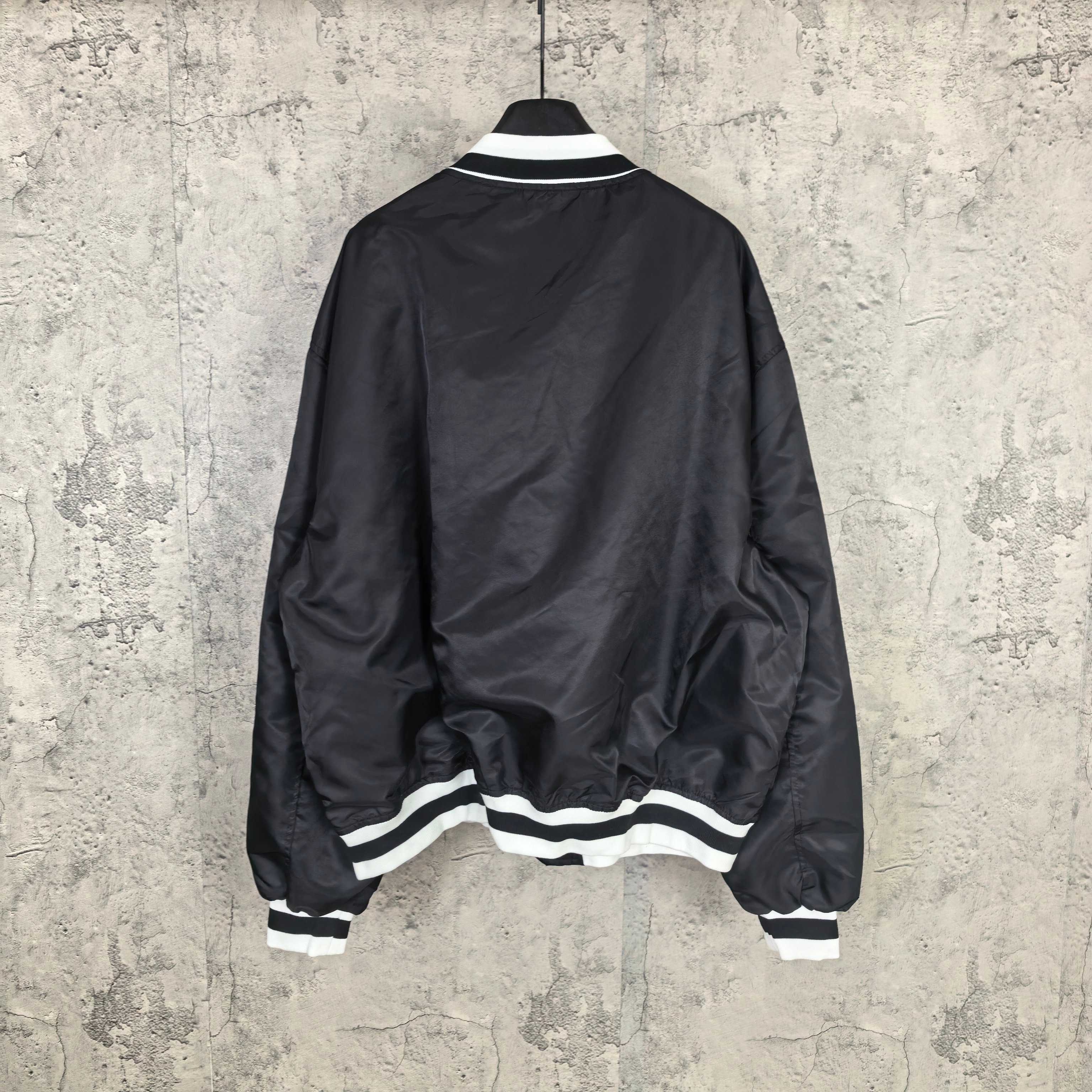 Black varsity bomber jacket, back view, with white striped ribbed hem