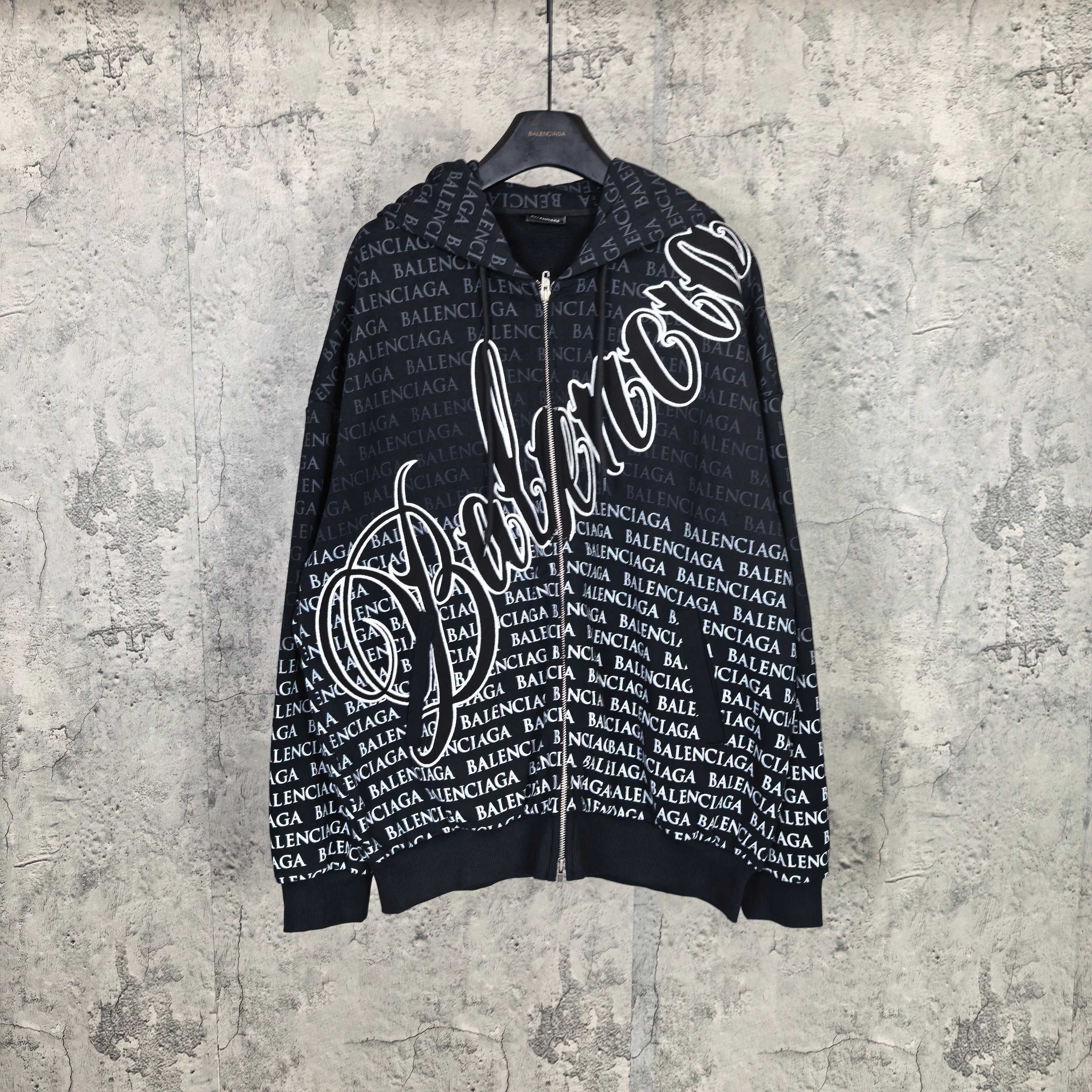 Long-sleeve zip hoodie in dark color, with allover Balenciaga text and graphic logo print.