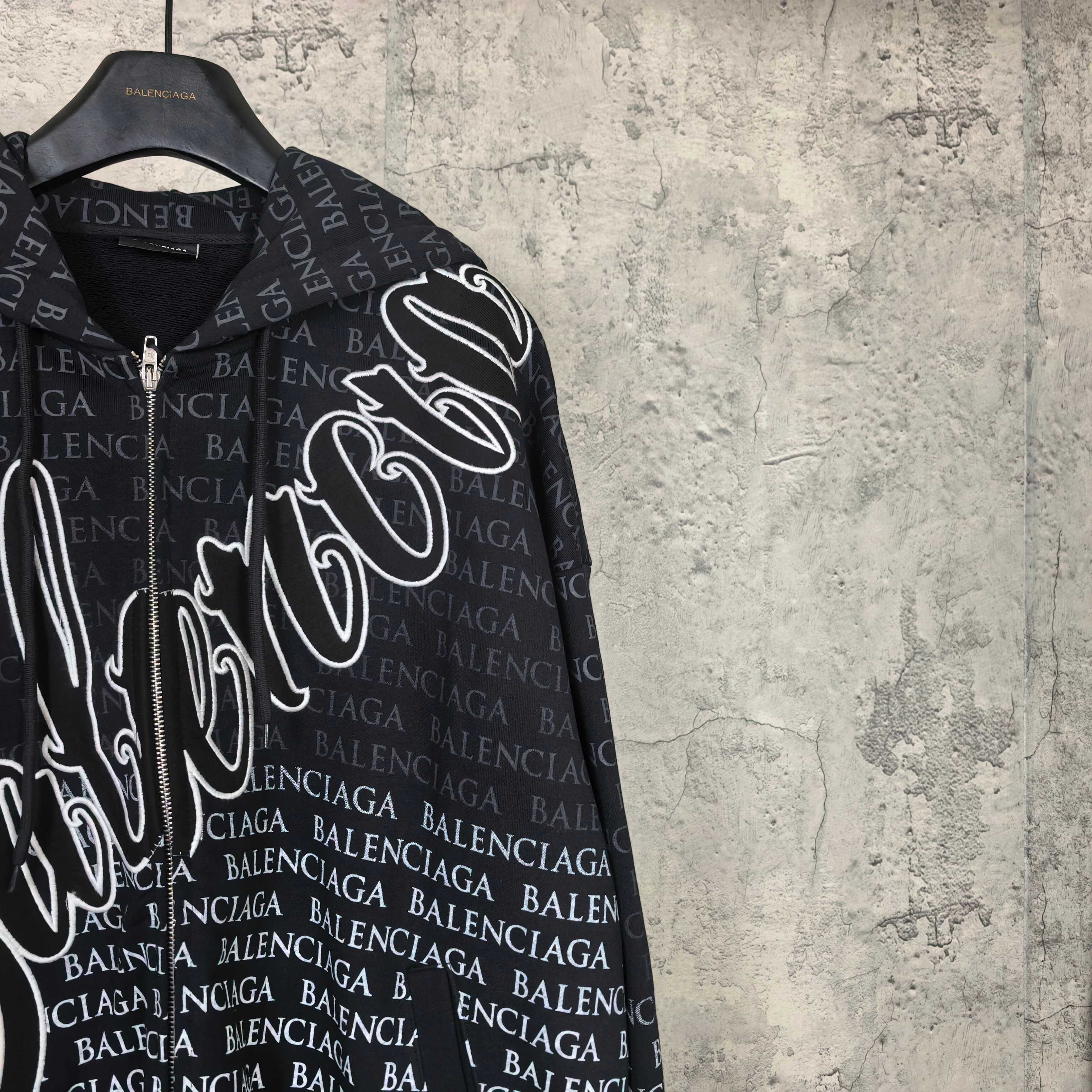 Balenciaga zip-up hoodie close-up, black with white logo graphic and repeating BALENCIAGA text
