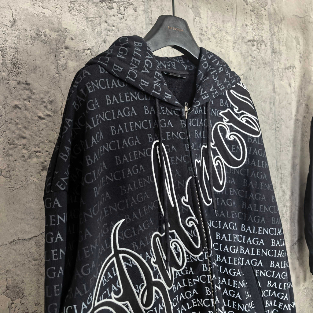 Front view of dark long-sleeve zip hoodie with hood and allover Balenciaga text print.